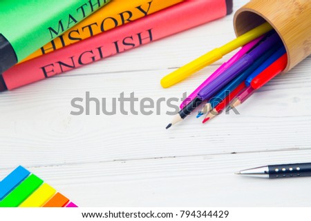Education concept. Studying for exams. A stack os student's books and a pencilcase with colored pencils and markers on a white wooden table, space for a text or product display