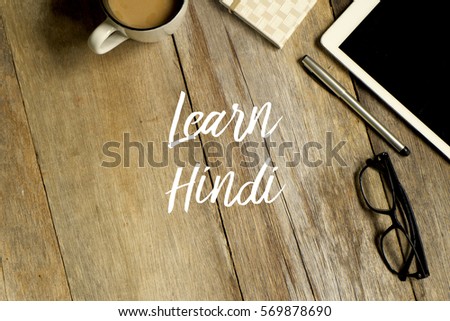 Education concept. Top view of tablet, glasses. notebook pen and a cup of coffee with LEARN HINDI written on wooden background.