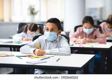 Education During Pandemic. Small Boy Sitting At Table In Classroom At School Or Kindergarten, Wearing Surgical Face Mask, Writing Or Drawing In Notebook. New Normal, Safe Learning