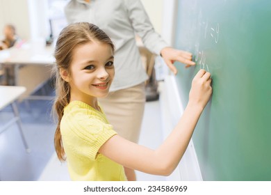 Education, Elementary School, Learning, Math And People Concept - Little Smiling Schoolgirl Writing Numbers On Green Chalk Board In Classroom