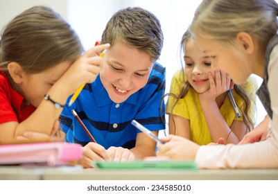 Education, Elementary School, Learning And People Concept - Group Of School Kids With Pens And Papers Writing In Classroom