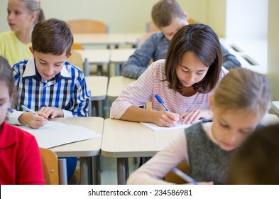 Education, Elementary School, Learning And People Concept - Group Of School Kids With Pens And Notebooks Writing Test In Classroom