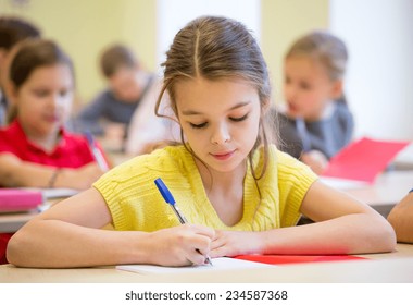 Education, Elementary School, Learning And People Concept - Group Of School Kids With Pens And Notebooks Writing Test In Classroom