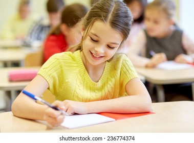 Education, Elementary School, Learning And People Concept - Group Of School Kids With Pens And Notebooks Writing Test In Classroom