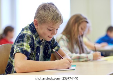 Education, Elementary School, Learning And People Concept - Group Of School Kids With Pens And Notebooks Writing Test In Classroom