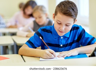 Education, Elementary School, Learning And People Concept - Group Of School Kids With Pens And Notebooks Writing Test In Classroom