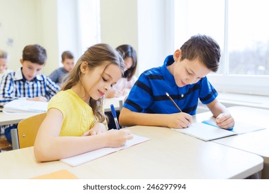 Education, Elementary School, Learning And People Concept - Group Of School Kids With Pens And Notebooks Writing Test In Classroom