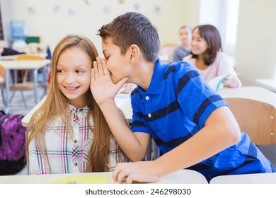 education, elementary school, learning and people concept - smiling schoolboy whispering secret to classmate ear in classroom - Powered by Shutterstock