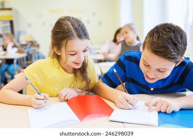 Education, Elementary School, Learning And People Concept - Group Of School Kids With Pens And Notebooks Writing Test In Classroom