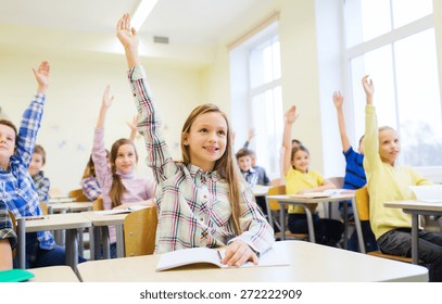 Education, Elementary School, Learning And People Concept - Group Of School Kids With Notebooks Sitting In Classroom And Raising Hands