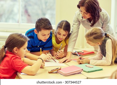 Education, Elementary School, Learning And People Concept - Teacher Helping School Kids Writing Test In Classroom