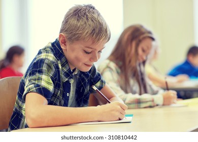 Education, Elementary School, Learning And People Concept - Group Of School Kids With Pens And Notebooks Writing Test In Classroom