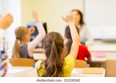 Education, Elementary School, Learning And People Concept - Group Of School Kids With Teacher Sitting In Classroom And Raising Hands