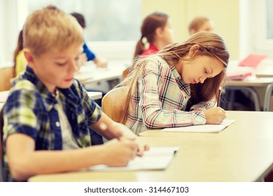 Education, Elementary School, Learning And People Concept - Group Of School Kids With Pens And Notebooks Writing Test In Classroom