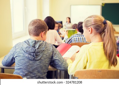 Education, Elementary School, Learning And People Concept - Group Of School Kids With Notebook Writing Test And Helping In Classroom