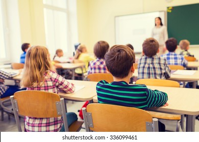 education, elementary school, learning and people concept - group of school kids sitting and listening to teacher in classroom from back - Shutterstock ID 336099461