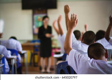 education, elementary school, learning and people concept - group of school kids with teacher standing in classroom and raising hands