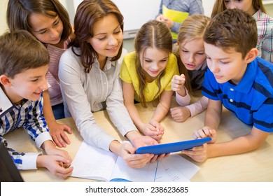 Education, Elementary School, Learning, Technology And People Concept - Group Of School Kids With Teacher Looking To Tablet Pc Computer In Classroom