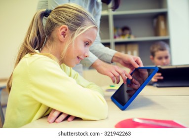 Education, Elementary School, Learning, Technology And People Concept - Little Girl With Teacher And Tablet Pc Computer In Classroom