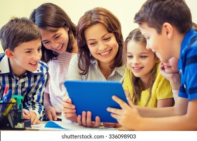 Education, Elementary School, Learning, Technology And People Concept - Group Of School Kids With Teacher Looking To Tablet Pc Computer In Classroom