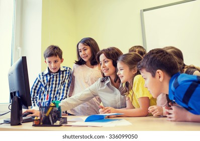 Education, Elementary School, Learning, Technology And People Concept - Group Of School Kids With Teacher Looking To Computer Monitor In Classroom