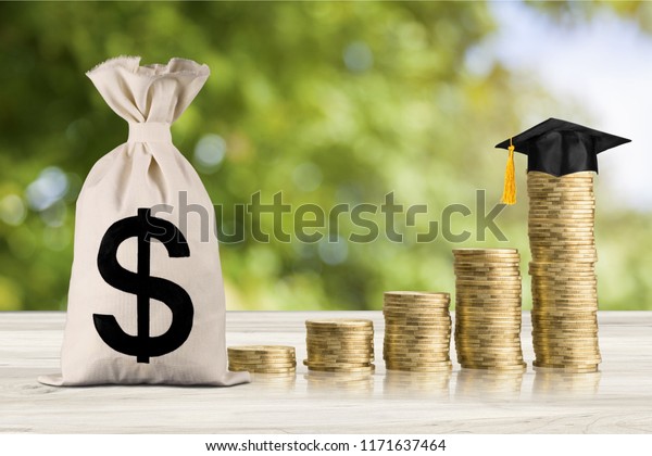 Education expense or student loan for post secondary\
education concept : Dollar bag, graduation cap on row of coins on a\
table, depicts loan or money designed to help students pay for\
associated fees