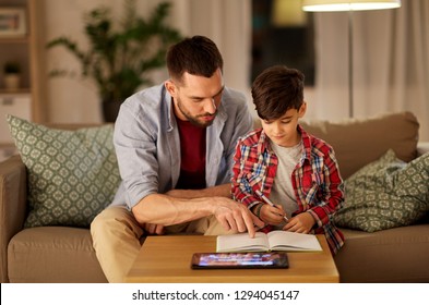 Education And Family Concept - Father And Son With Book And Tablet Computer Doing Homework Together At Home In Evening