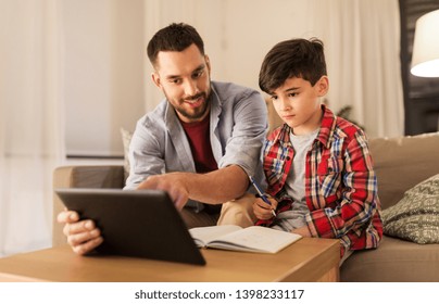 Education, Family And Homework Concept - Happy Father And Son With Tablet Computer Writing To Notebook At Home