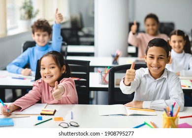 Education Is Fun Concept. Diverse group of happy smiling international classmates sitting at desks in classroom and showing thumbs up sign gesture, children enjoying studying at junior school - Powered by Shutterstock