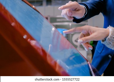 Education, futuristic and technology concept - woman and man using interactive touchscreen display of red electronic kiosk at technology exhibition - scrolling and touching