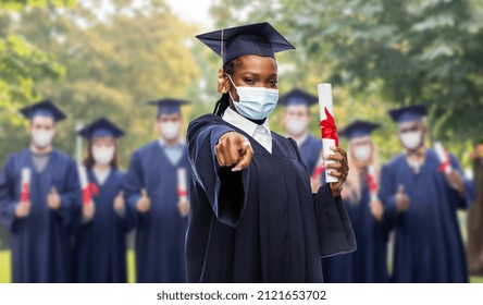 Education, Graduation And Pandemic Concept - Graduate Student Woman In Mortarboard And Bachelor Gown With Diploma Wearing Protective Mask Pointing To Camera Over Group Of People On Background