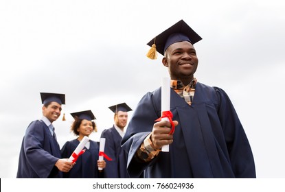 education, graduation and people concept - happy african american graduate in mortar boards and bachelor gown with diploma and group of international students