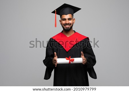 education, graduation and people concept - happy smiling indian male graduate student in mortar board and bachelor gown with diploma over grey background