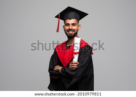 education, graduation and people concept - happy indian male graduate student in mortar board and bachelor gown with diploma over grey background