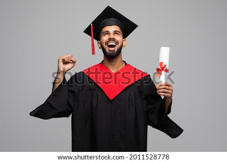 education, graduation and people concept - happy smiling indian male graduate student in mortar board and bachelor gown with diploma celebrating success over grey background