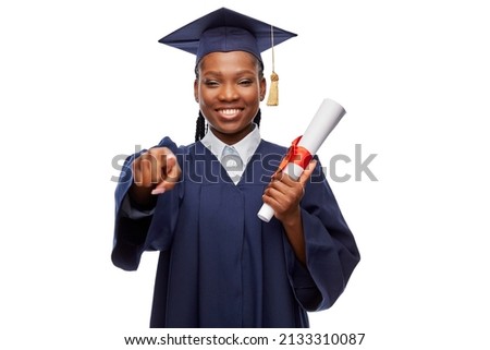 education, graduation and people concept - happy graduate student woman in mortarboard and bachelor gown with diploma pointing finger to camera over white background