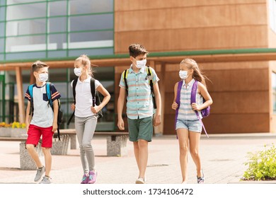 Education, Healthcare And Pandemic Concept - Group Of Elementary School Students Wearing Face Protective Medical Masks For Protection From Virus Disease With Backpacks Walking And Talking Outdoors