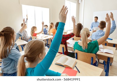 Education, High School, Teaching, Learning And People Concept - Group Of Happy Students Raising Hands And Teacher In Classroom