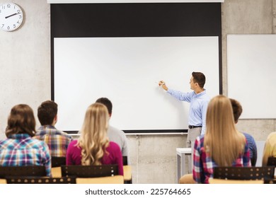 Education, High School, Teamwork And People Concept - Smiling Teacher Standing In Front Of Students And Writing Something On White Board In Classroom