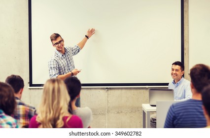 education, high school, technology and people concept - student standing with remote control, laptop computer in front of teacher and classmates in classroom