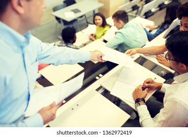 Education, High School, University, Learning And People Concept - Teacher Giving Exam Tests To Students At Lecture Hall