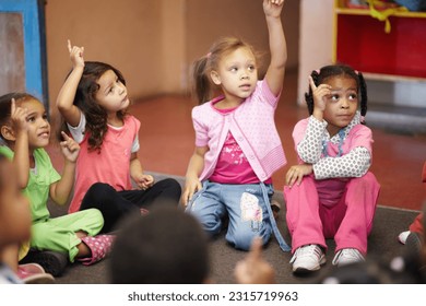 Education, kindergarten and kids asking a question with hands raised while sitting on a classroom floor for child development. School, learning or curiosity with children in class to study for growth - Shutterstock ID 2315719963