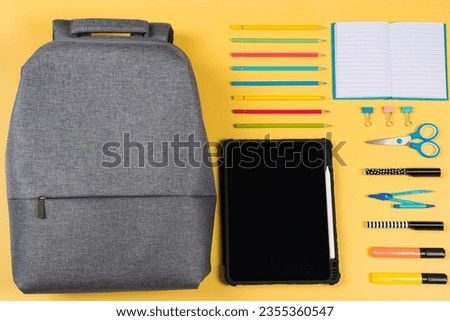 Education, learning, back to school background. Knolling composition with gray backpack and different school stationery supplies on yellow background. Top view, flat lay