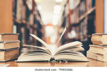 Education learning concept with opening book or textbook in old library, stack piles of literature text academic archive on reading desk and aisle of bookshelves in school study class room background
