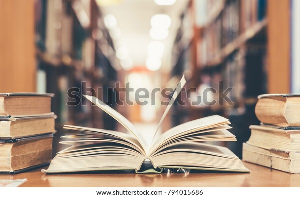 Education learning concept with opening book\
or textbook in old library, stack piles of literature text academic\
archive on reading desk and aisle of bookshelves in school study\
class room background
