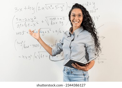 Education And Learning Concept. Portrait of smiling Arabian female teacher standing at whiteboard, explaining math calculations to students. Excited woman in glasses looking at camera, writing. - Powered by Shutterstock