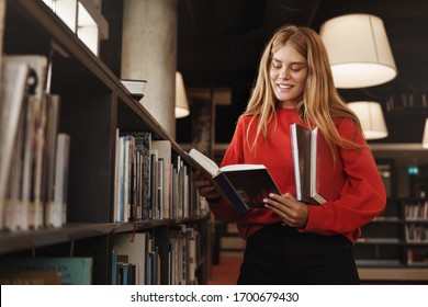 Education, learning and personal growth concept. Attractive redhead girl, student standing in library near shelves, reading book and smiling, studying, pick novel in bookstore, prepare homework