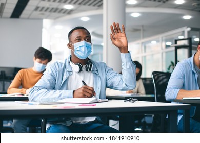 Education, Pandemic And Health Concept. African American Male Student Raising Hand For Answer, Wearing Protective Medical Mask For Protection From Virus Disease At High School Lesson. New Normal