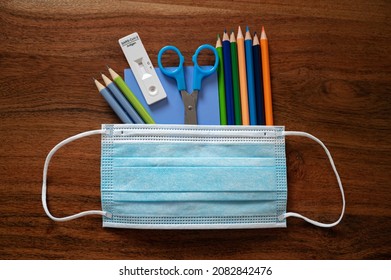 Education And School During Coronavirus Pandemic Conceptual Image - Medical Protective Mas Over Notepad And Color Pencils Along With Self Covid19 Test Stick.