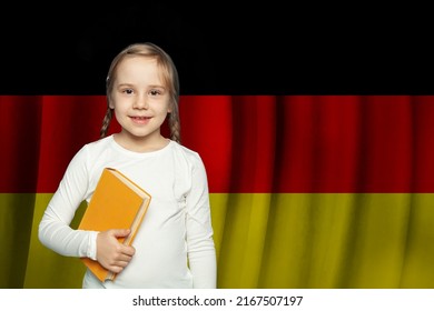 Education and school in Germany. Beautiful cute little kid girl with book against German flag background. 